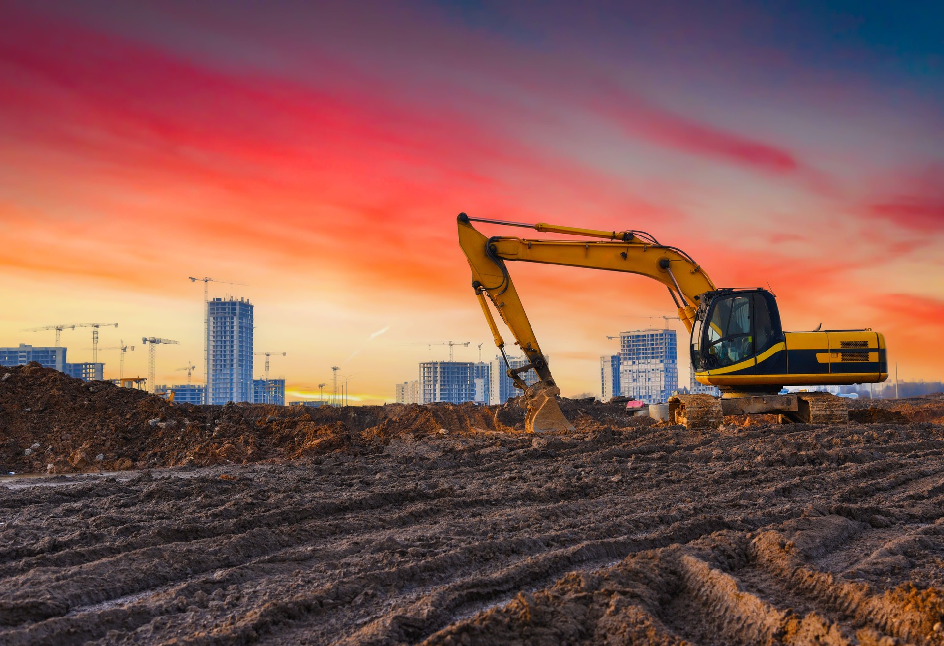 Excavator on construction site. Buildings under construction on sunset.