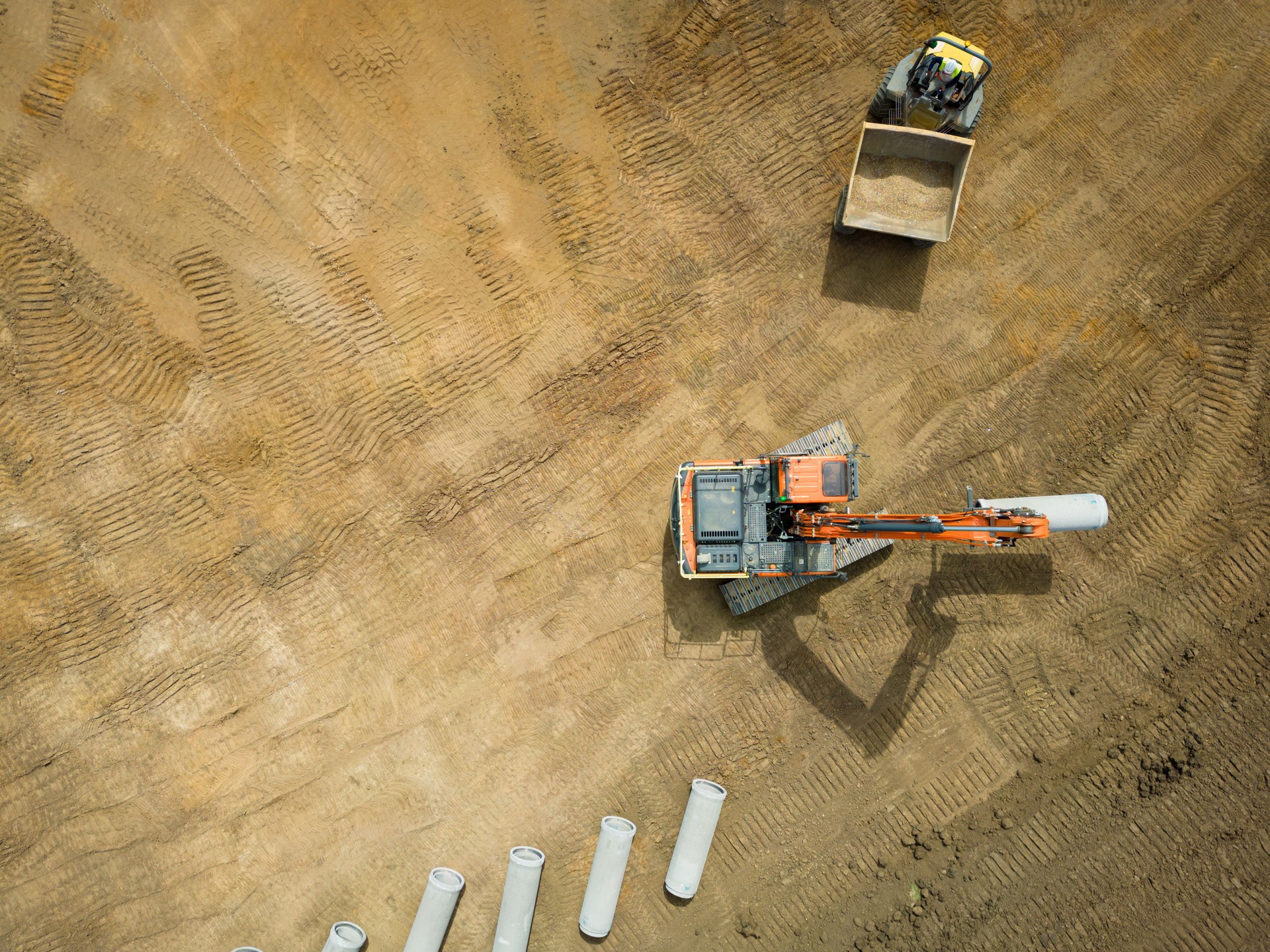 UAV view of an excavator seen taking part of a water pipe from a dumper truck.
